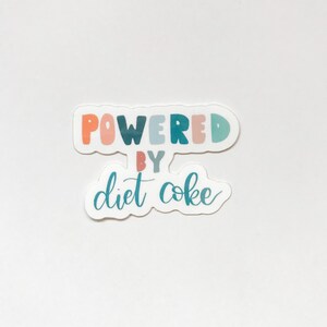 May include: A sticker with the text "Powered by Diet Coke" in colorful letters. The words "Powered" and "by" are in a rainbow of colors, and "Diet Coke" is in a teal blue.