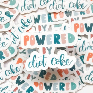 May include: A collection of stickers with the phrase "Powered by Diet Coke" in colorful, bubbly letters. The stickers are on a white background and feature various designs, including the words "Diet Coke" and "Powered by" in different fonts and colors.