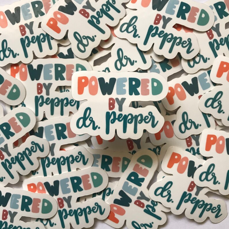 May include: A collection of white stickers with the text "POWERED BY dr. pepper" in various colors. The stickers have a rounded shape and are scattered across a white surface. The text is in a playful, handwritten style.