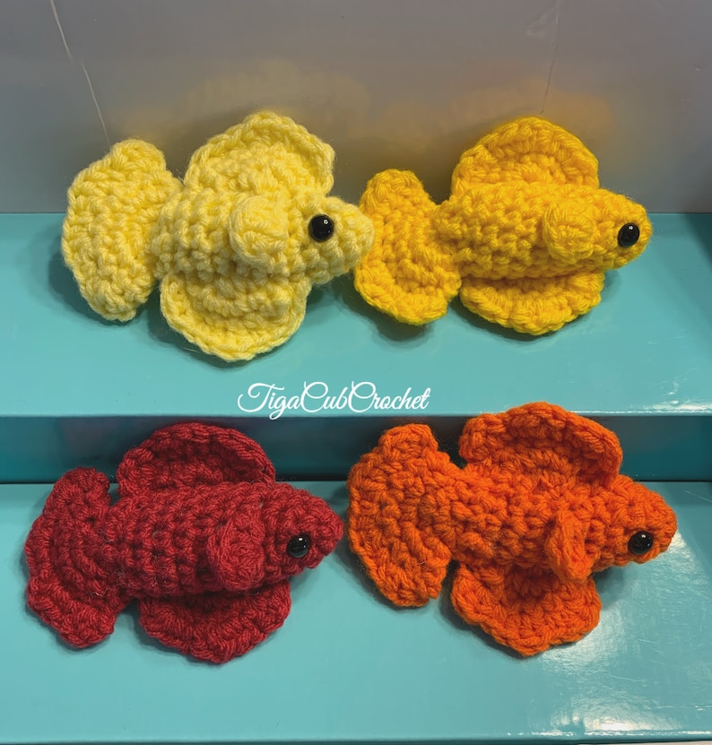 May include: Three crocheted betta fish, one yellow, one orange, and one red. The fish are all in a similar pose with their fins spread out. The fish are all about 3 inches long.