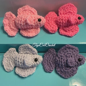 May include: Four crocheted betta fish, two pink, one light purple, and one gray. The fish are all in a similar pose with their fins spread out. The fish are all about 3 inches long.