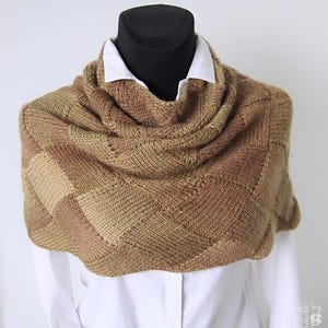 May include: A brown and beige knitted scarf with a geometric pattern. The scarf is folded and draped over a white shirt.