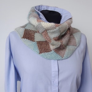May include: A light blue collared shirt with a brown, beige, and blue knitted cowl neck scarf. The scarf is made of different coloured squares.