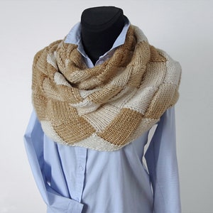 May include: A brown and white knitted infinity scarf with a chequered pattern. The scarf is draped over a mannequin wearing a light blue shirt.