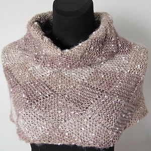 May include: A hand-knitted cowl in shades of brown, beige, and purple, with white flecks throughout. The cowl features a high, rolled turtleneck and a textured knit pattern. The garment is displayed on a black mannequin.