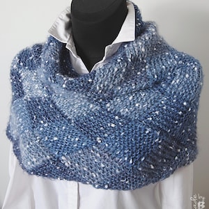 May include: A blue and white knitted cowl with a speckled pattern. The cowl is draped over a white shirt on a mannequin.