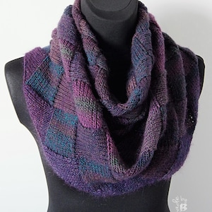 May include: A purple, blue and green knitted infinity scarf with a textured pattern. The scarf is displayed on a black mannequin.