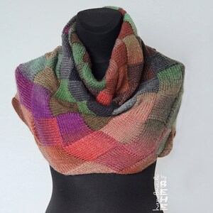 May include: A handmade, multi-coloured cowl scarf displayed on a black mannequin. The scarf features a patchwork design with squares of purple, green, red, brown, and grey. The cowl is thick and appears to be knitted or crocheted.