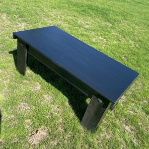 May include: A black wooden coffee table with a rectangular top and simple legs. The table is sitting on a green grassy lawn.