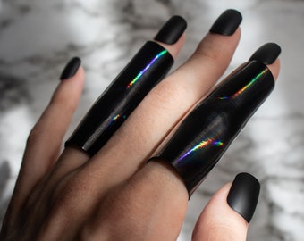 May include: A hand wearing two black iridescent rings on the middle and index fingers. The rings are wide and cover most of the finger.