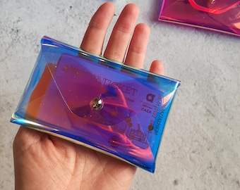 May include: A clear iridescent plastic envelope with a silver button closure. The envelope has a printed design of a bus ticket with the text "ATENA TICKET" and a date of "05/01/2022".