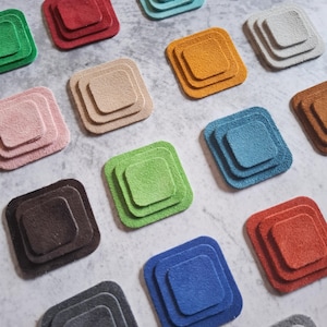 Puede incluir: Un surtido de posavasos cuadrados y coloridos en varios tonos, incluyendo verde, rojo y azul. Cada posavasos está compuesto por tres cuadrados anidados, creando un efecto de capas. Los posavasos están dispuestos sobre una superficie gris claro.