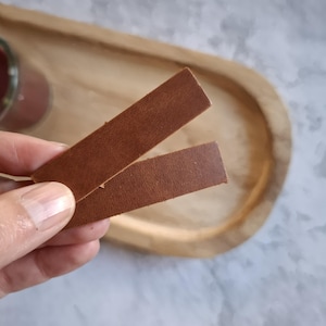 Op de afbeelding: Twee bruine leren stroken, een bovenop de andere, op een houten oppervlak.