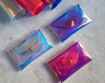 May include: Four iridescent clear plastic envelopes with a gold button closure. The envelopes are in shades of blue, purple, and pink.