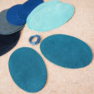 Puede incluir: Piezas de cuero de gamuza ovaladas en varios tonos de azul y turquesa, con agujeros pre-perforados para coser. También hay un pequeño carrete de hilo azul. Estas piezas son probablemente para proyectos de artesanía o marroquinería.