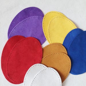 May include: A collection of oval-shaped leather pieces in various colors, including red, purple, yellow, blue, white, and brown. Each piece has a series of small, evenly spaced holes around the edge, suggesting they are designed for stitching or crafting projects.