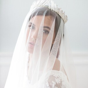 May include: A bride wearing a white veil and a crystal crown. The veil is sheer and covers most of her face.