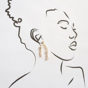 May include: A line drawing of a person's face with a pair of pearl and gold hoop earrings. The earrings are shaped like an arch and are made of small pearls.
