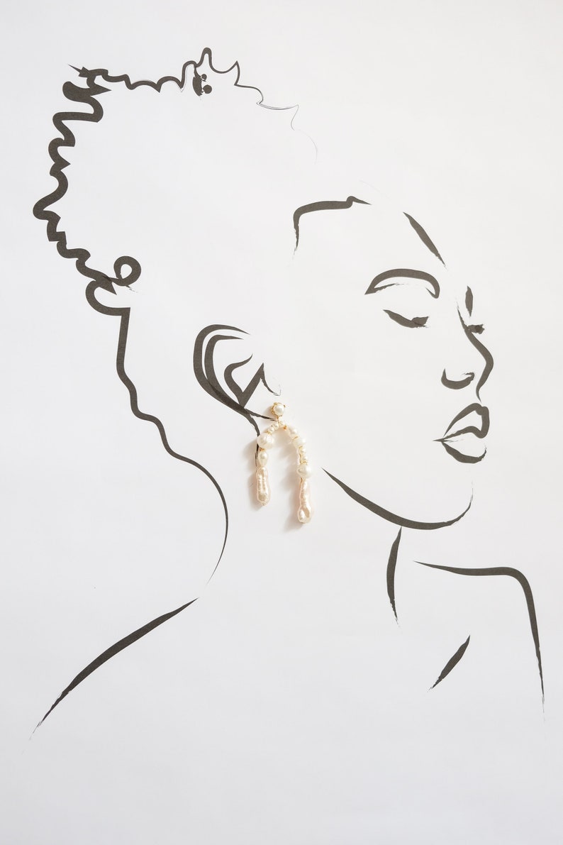 May include: A line drawing of a person's face with a pair of pearl and gold hoop earrings. The earrings are shaped like an arch and are made of small pearls.
