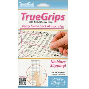 Peut inclure: Un paquet d'anneaux adhésifs antidérapants TrueGrips pour règles. L'emballage montre une main plaçant un anneau sur une règle. Le texte sur l'emballage indique "TrueGrips Anneaux adhésifs antidérapants Appliquer à l'arrière de n'importe quelle règle ! Fini le glissement ! Le paquet contient 15 grands + 15 petits The Grace Company Fine Quilting Products"