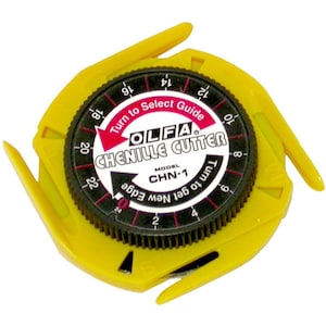 Peut inclure: Un cutter chenille Olfa jaune, modèle CHN-1, avec un cadran noir avec des chiffres et du texte. Le cadran indique "Turn to Select Guide" et "Turn to get New Edge". Le cutter a une forme unique en étoile.