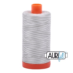 Peut inclure: Une bobine de fil blanc avec des rayures grises, enroulée sur une bobine en plastique avec un dessus et un dessous orange. La bobine est étiquetée "Aurifil" en lettres bleues.