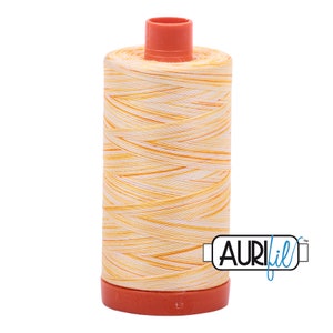 Peut inclure: Une bobine de fil Aurifil dans un coloris chiné jaune et blanc. La bobine est étiquetée "Aurifil" et possède un capuchon en plastique rouge.