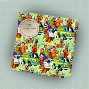 May include: A folded fabric featuring a colorful cartoon pattern with characters, a van, ghosts, and stars on a light green background. The fabric has the text "Koo Koo Nest Fabrics" and "Made with Love" on a circular label.