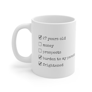 May include: White ceramic mug with a black checklist that reads: "27 years old", "money", "prospects", "burden to my parents", and "frightened".
