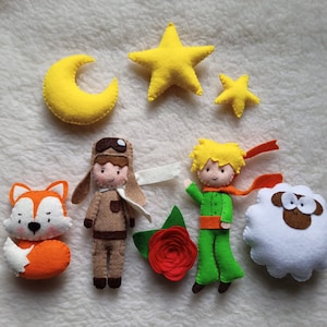Può includere: Set di giocattoli in feltro con i personaggi de Il Piccolo Principe, tra cui il principe, una volpe, una pecora, un pilota, una rosa, una luna crescente e due stelle. I personaggi sono tutti in feltro e hanno dettagli ricamati.
