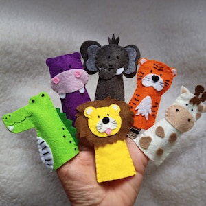 Op de afbeelding: Een set van zes vingerpoppen van vilt met verschillende dieren, waaronder een leeuw, een giraffe, een nijlpaard, een krokodil, een olifant en een tijger. De poppen zijn allemaal felgekleurd en hebben vriendelijke gezichten.