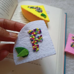 May include: A set of felt bookmarks with colorful embroidered letters. The letters are F and E, and the bookmarks are in white, yellow, and pink.