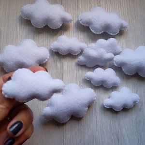 Könnte beinhalten: Zehn weiße Filz-Wolken in verschiedenen Größen. Die Wolken sind auf einer hellbraunen Holzoberfläche angeordnet.