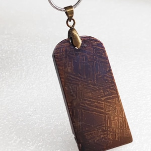 May include: A silver chain necklace with a rectangular pendant made of a dark brown metal with a textured surface. The pendant has a brass bail.