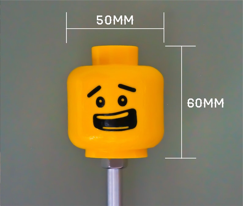 K&ouml;nnte beinhalten: Ein gelber LEGO Minifigurenkopf mit einem l&auml;chelnden Gesicht und hochgezogenen Augenbrauen. Der Kopf ist 5 cm breit und 6 cm hoch.