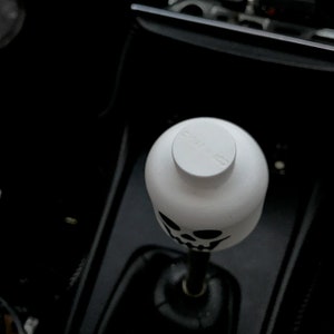 May include: White skull-shaped gear shift knob with a black skull design. The knob has a white top with the word "SHIFTED" printed on it.