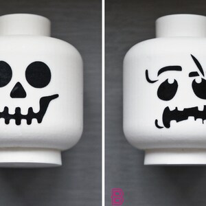 May include: Two white Lego minifigure heads with black Halloween-themed designs. One head has a skull design and the other has a spooky face.