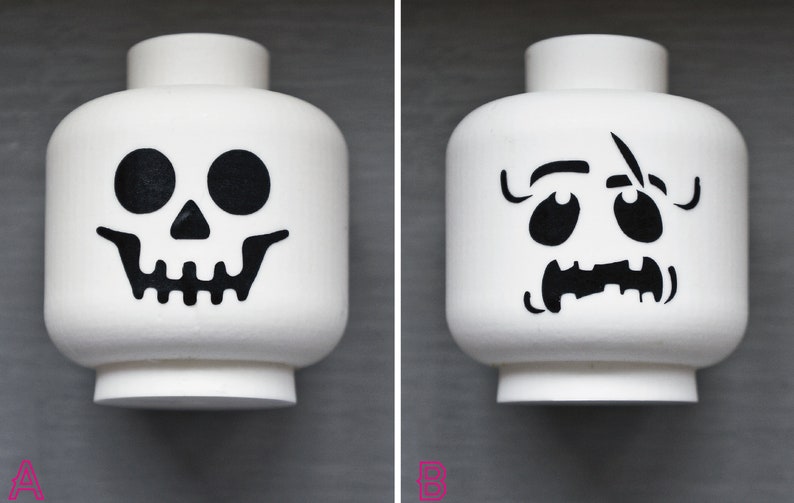 May include: Two white Lego minifigure heads with black Halloween-themed designs. One head has a skull design and the other has a spooky face.