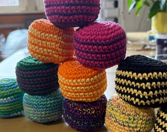 May include: A collection of eleven round, crocheted balls stacked in a pyramid shape. The balls feature various color combinations, including solid purple, orange, green, blue, black and yellow stripes, and multi-colored speckled yarn patterns.