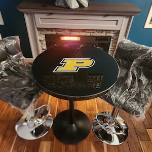 May include: A black and gold bar table with a black top featuring a yellow "P" logo. Two black bar stools with chrome bases surround the table.