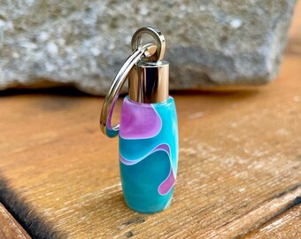 May include: A teal, pink, and white swirl patterned keychain with a silver metal ring and cap.