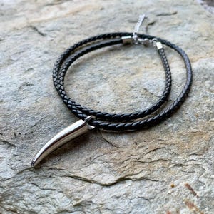 May include: A black leather cord necklace with a silver pendant shaped like a pointed tooth.