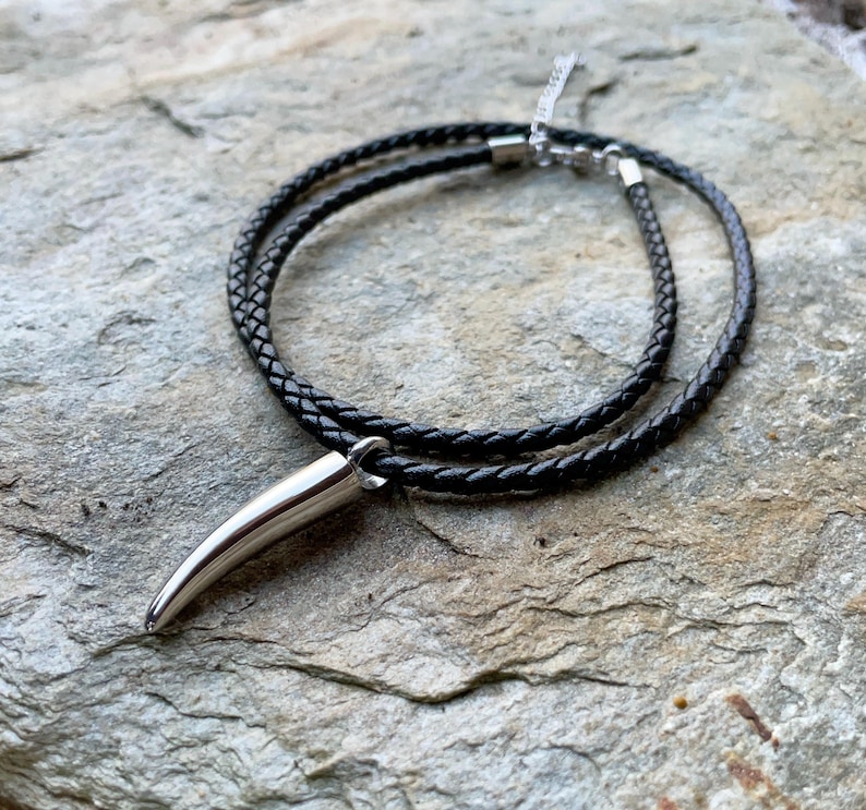 May include: A black leather cord necklace with a silver pendant shaped like a pointed tooth.