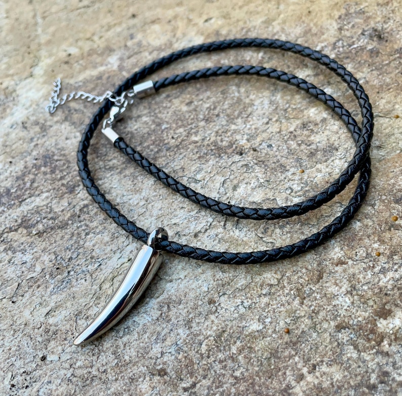 May include: A black leather cord necklace with a silver tooth pendant.