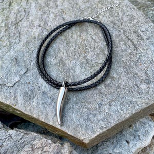 May include: A black leather cord necklace with a silver, pointed pendant shaped like a tooth.