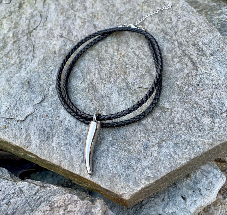 May include: A black leather cord necklace with a silver, pointed pendant shaped like a tooth.