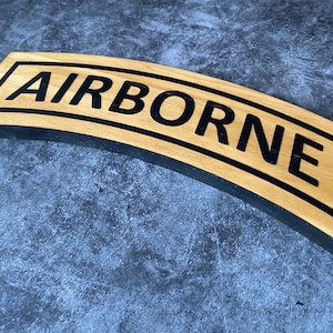 May include: A wooden sign with a black border and the word "AIRBORNE" in black lettering.