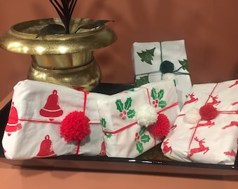 Puede incluir: Cuatro regalos de Navidad envueltos en papel blanco con diferentes diseños festivos. Los regalos están decorados con pompones rojos y blancos.