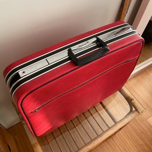 Peut inclure: Valise vintage rouge avec des rayures noires et une garniture en métal argenté. La valise a une poignée noire et le mot "Airline" est imprimé sur le dessus.