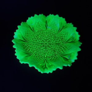 Könnte beinhalten: Eine leuchtend grüne Glasschale mit einem detaillierten, strukturierten Muster. Die Schale hat einen gewellten Rand und ein zentrales Sternmuster. Das Glas scheint vintage zu sein, mit einer lebendigen, fast neonfarbenen grünen Farbe vor schwarzem Hintergrund.